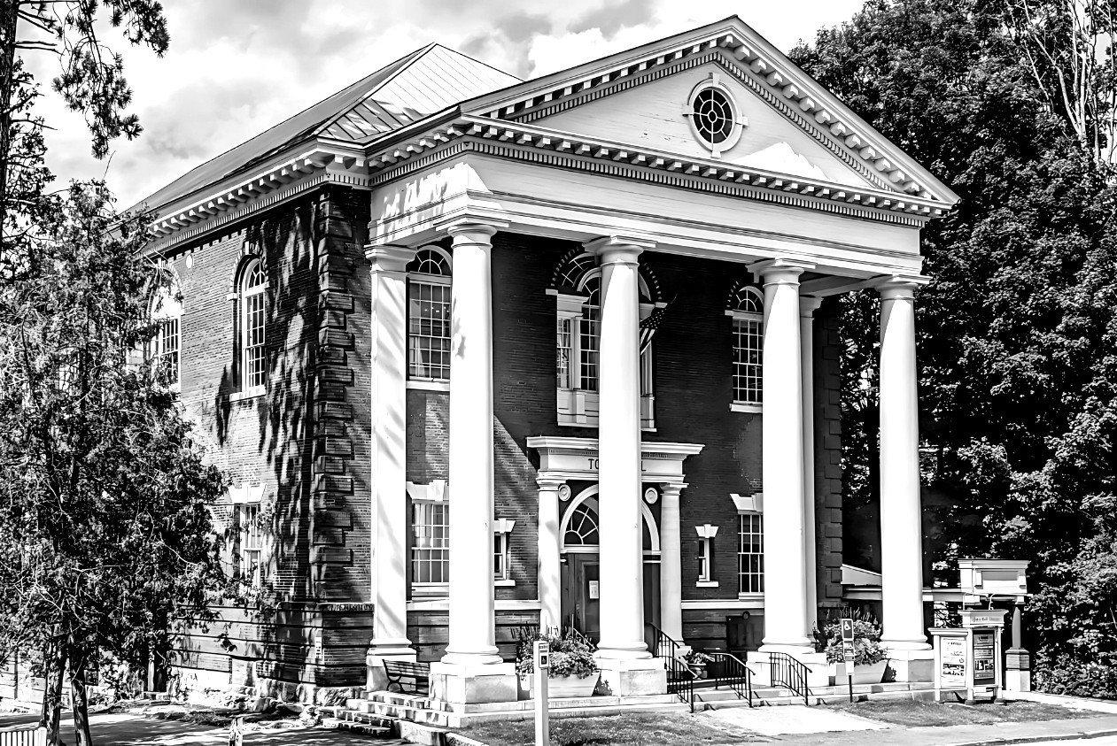 Black-and-white photograph of the Woodstock Town Hall on The Green: a columned portico with a triangular pediment and round upper window, framed by trees