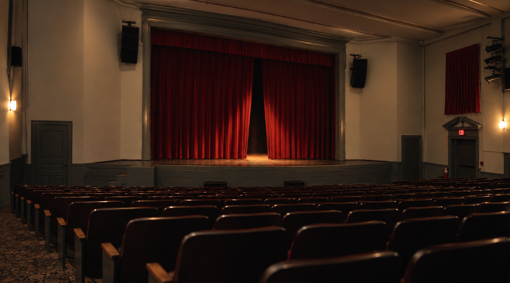 The auditorium of the Woodstock Town Hall Theatre moments before a show: dark wooden seats angle toward the stage, where the red curtain is just beginning to open