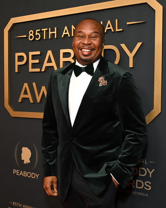 Roy Wood Jr. smiling in a black tuxedo on the red carpet at the 85th Annual Peabody Awards.
